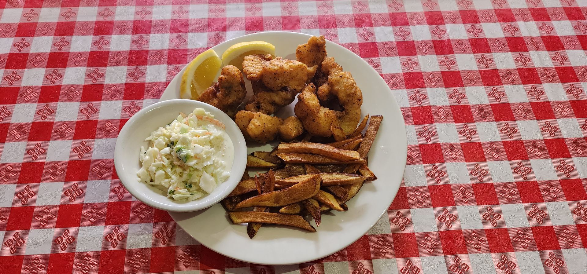 A plate of food with french fries and coleslaw on a checkered table cloth.