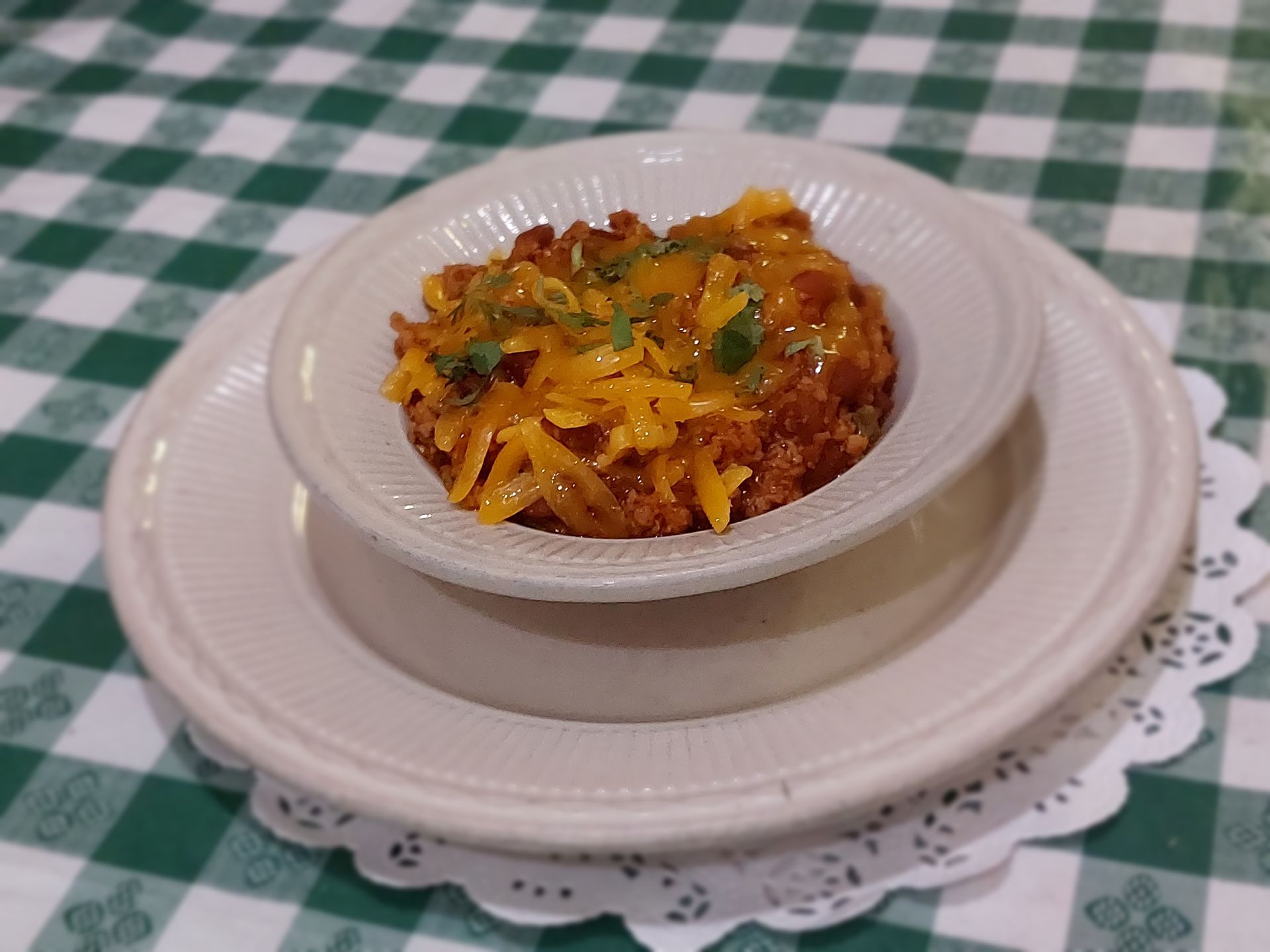 A white plate topped with a bowl of food on a checkered table cloth.