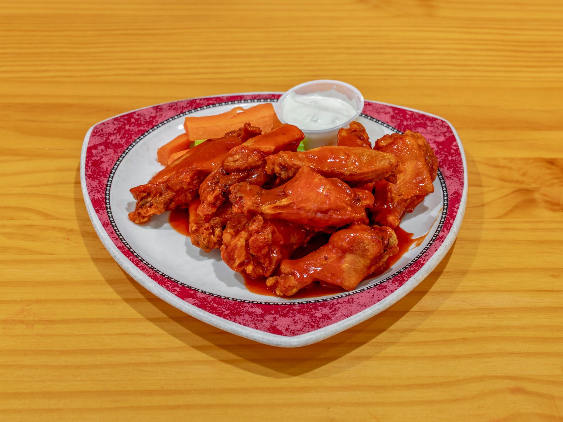 A plate of chicken wings with carrots and ranch dressing on a wooden table.