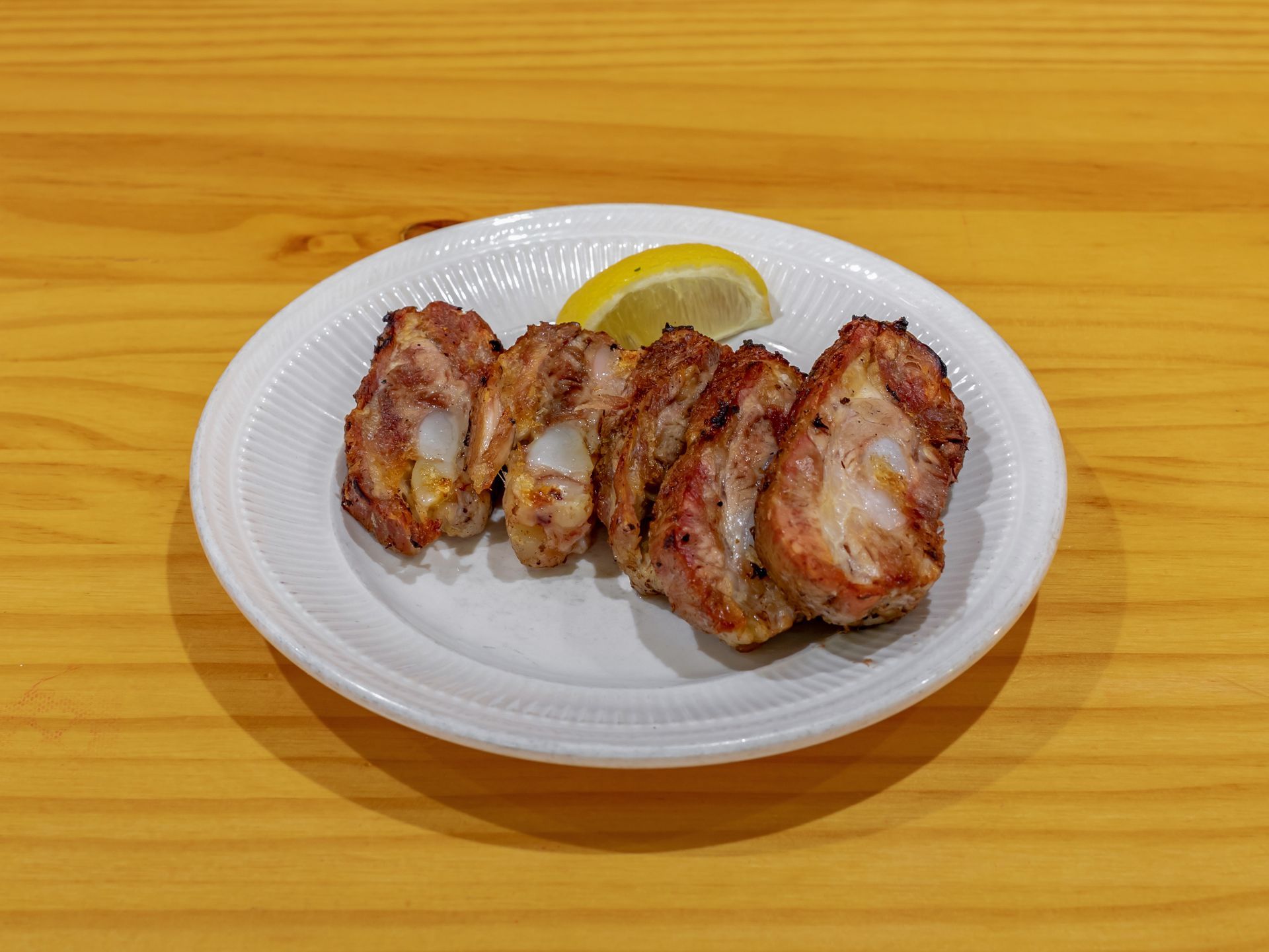 A white plate topped with meat and a slice of lemon on a wooden table.