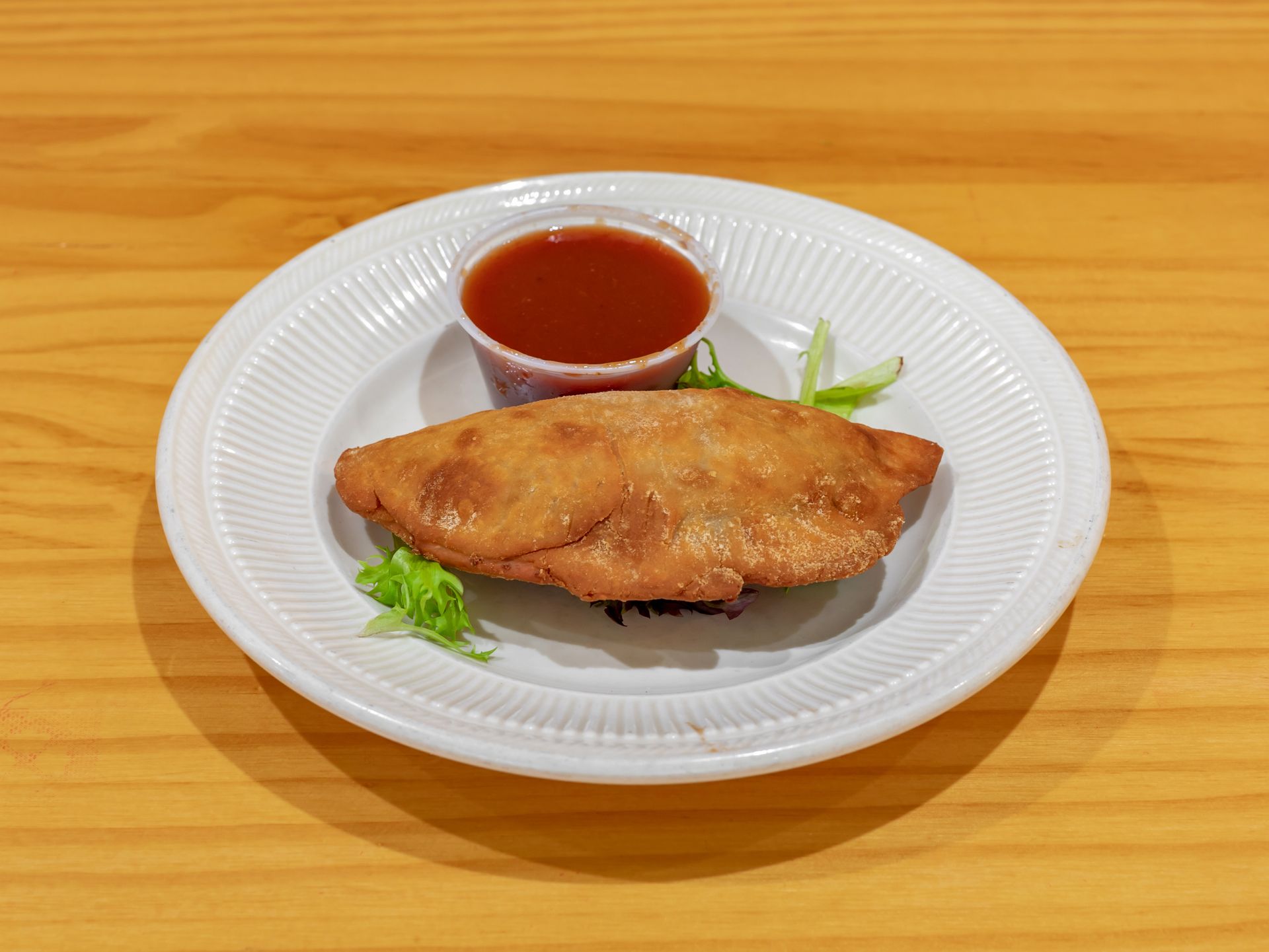 A white plate topped with fried food and a small cup of sauce.