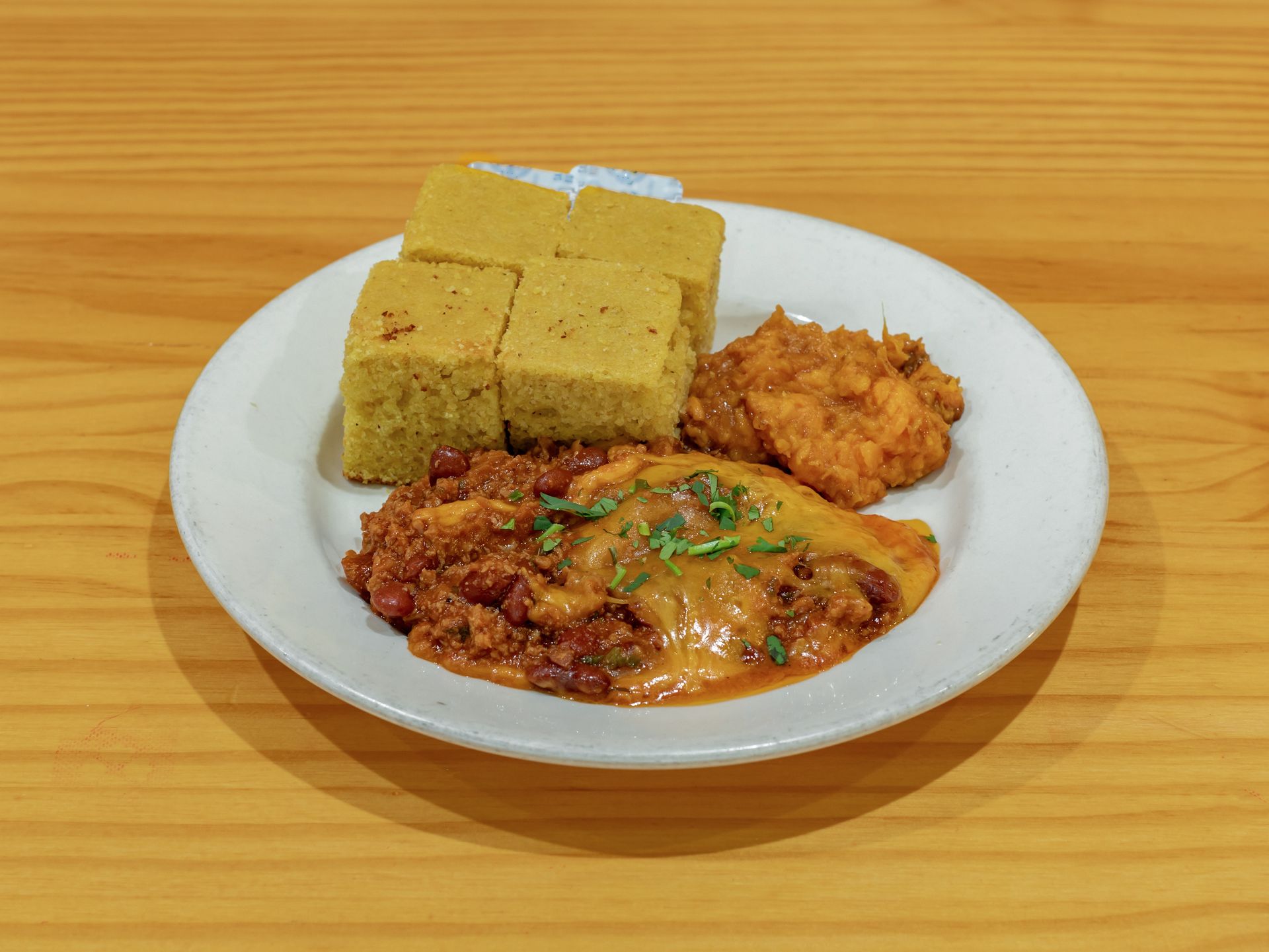 A plate of food with cornbread and beans on a wooden table.