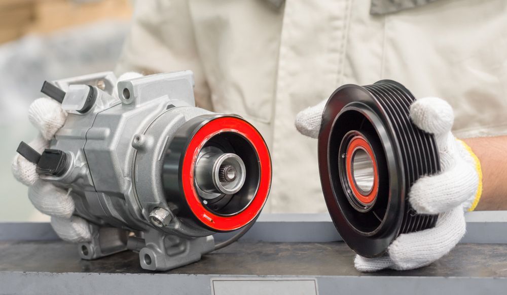 A Person Is Holding A Compressor And A Pulley In Their Hands — Bowen Automotive In Bowen, QLD