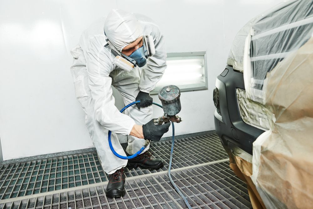 Person in Protective Suit Painting a Car Bumper in a Paint Booth — Bowen Automotive in Bowen, QLD