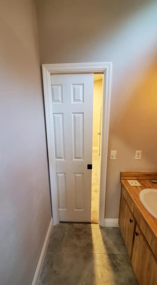A white pocket door partially open to reveal a lit interior, situated next to a wooden vanity in a room with gray flooring.