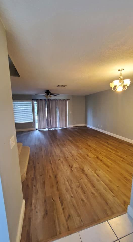 Spacious open-concept living area with light wood floors, a ceiling fan, sliding glass doors, and a decorative chandelier.