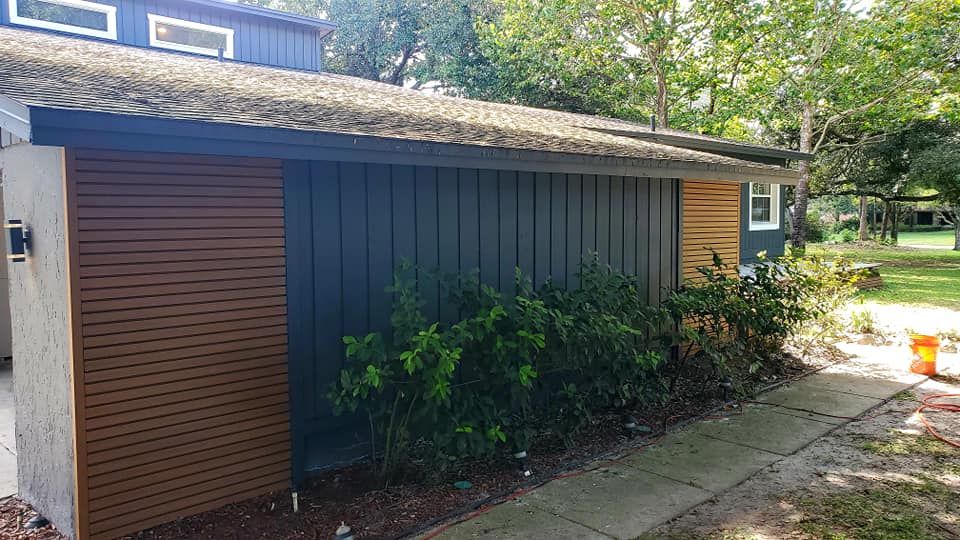 A modern home exterior with dark grey vertical siding, horizontal wood slat accent walls, and green shrubs in the yard.