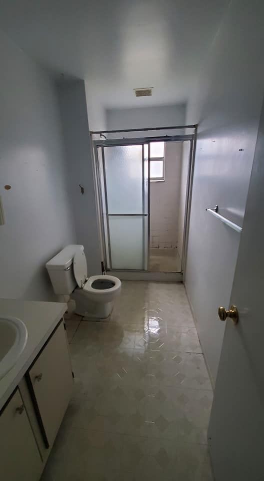 A small bathroom with a white toilet, a vanity sink on the left, and a sliding glass shower stall at the far end.