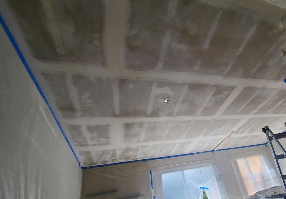 A ceiling under renovation with visible drywall joints taped and mudded, surrounded by blue painter's tape and plastic.