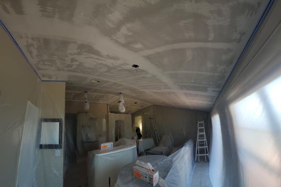 Interior view of a residential room during ceiling renovation, with taped joints, plastic sheeting, and a step ladder.