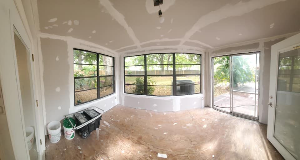 An interior view of a sunroom under construction with unfinished drywall, windows, and a sliding glass door.
