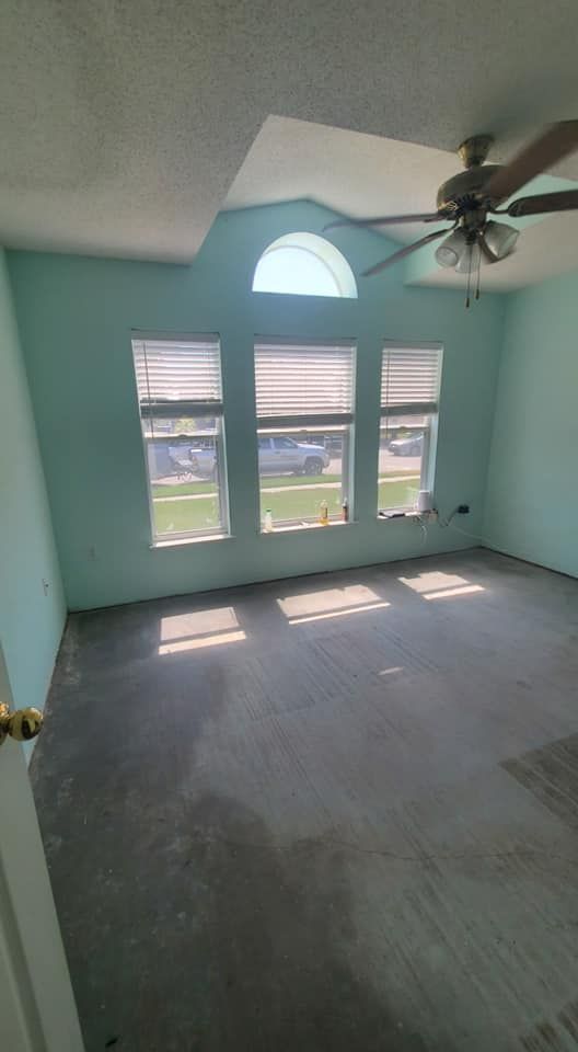 Empty room with light blue walls, gray carpet, three tall windows, a semi-circular transom window, and a ceiling fan.