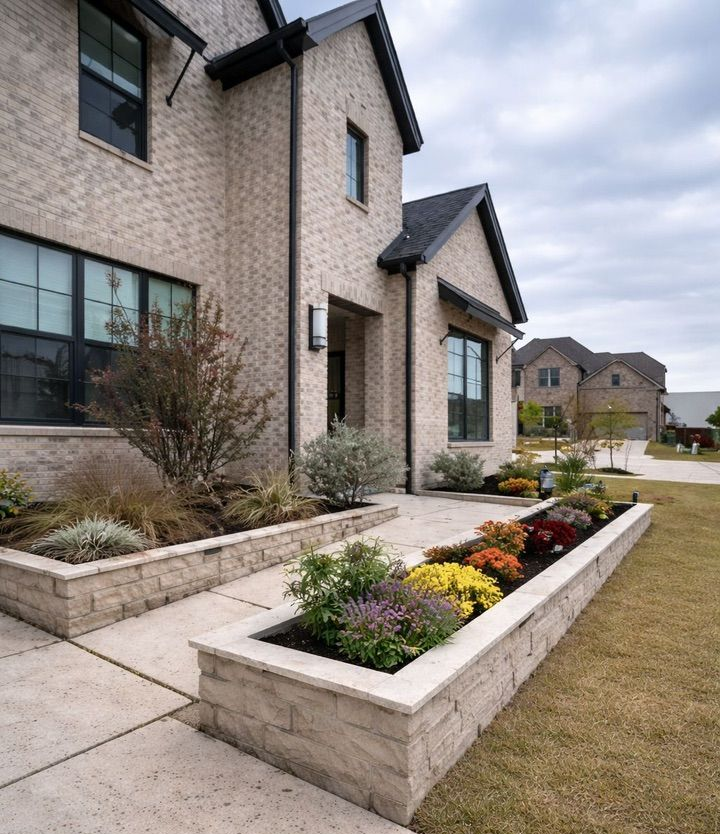 Wavy brick retaining wall bordering a flower bed with plants, and lush green grass.