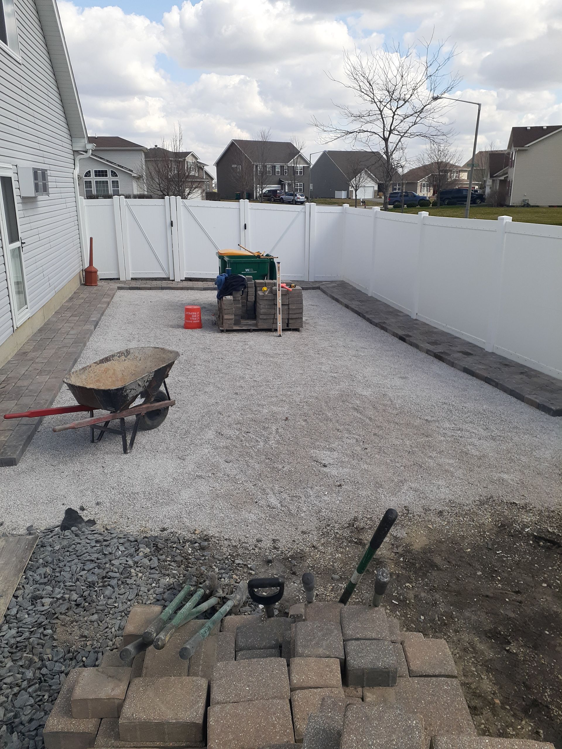 A wheelbarrow is sitting on top of a pile of gravel in a backyard.