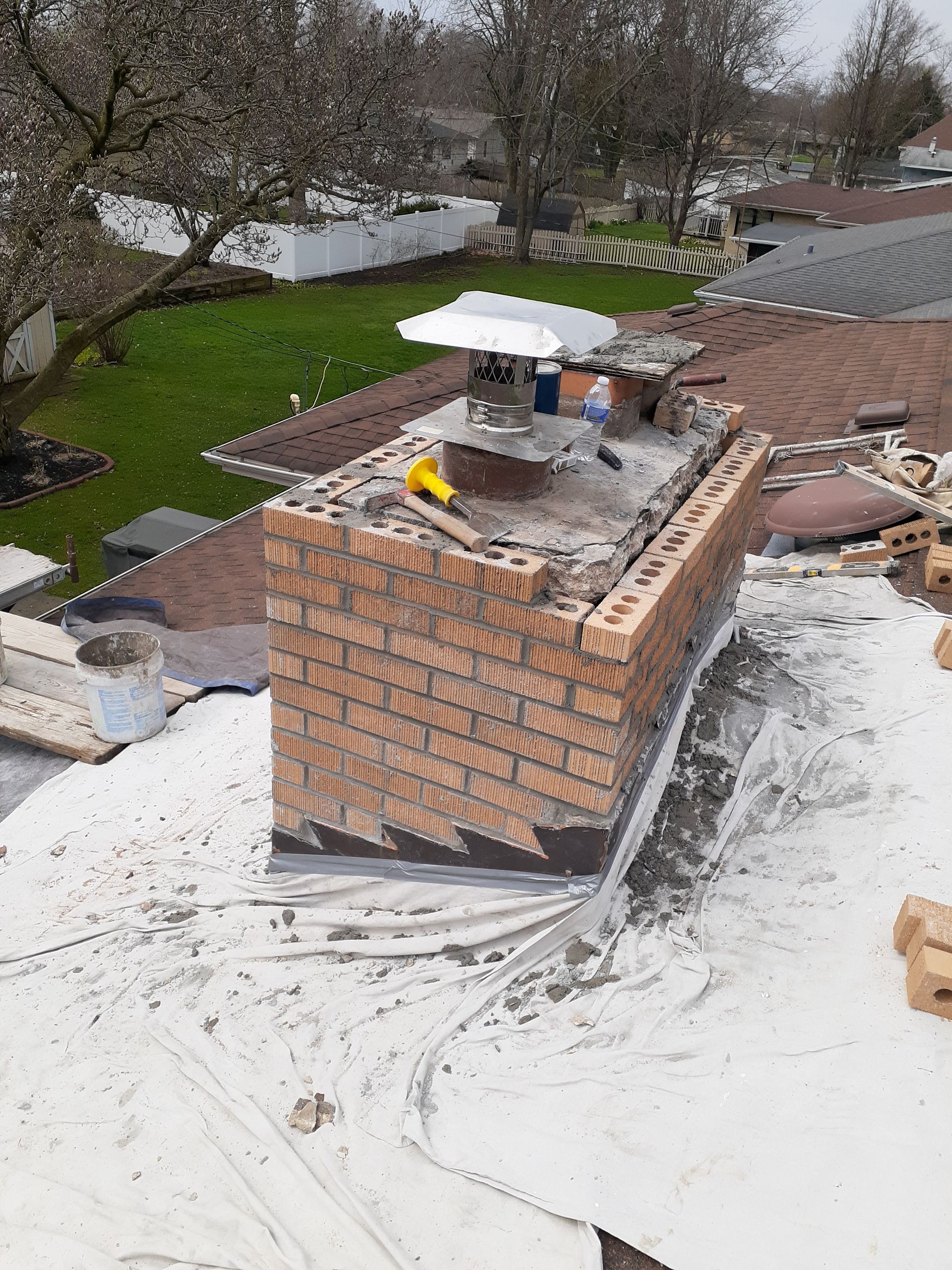An aerial view of a brick chimney being built on top of a roof.