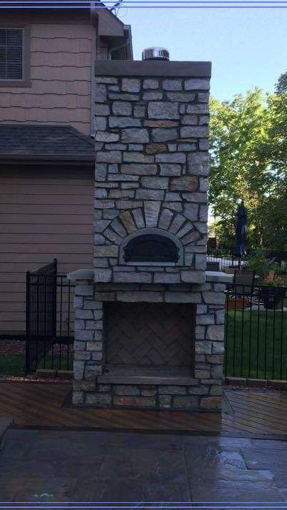 A stone fireplace with a pizza oven in the backyard of a house.