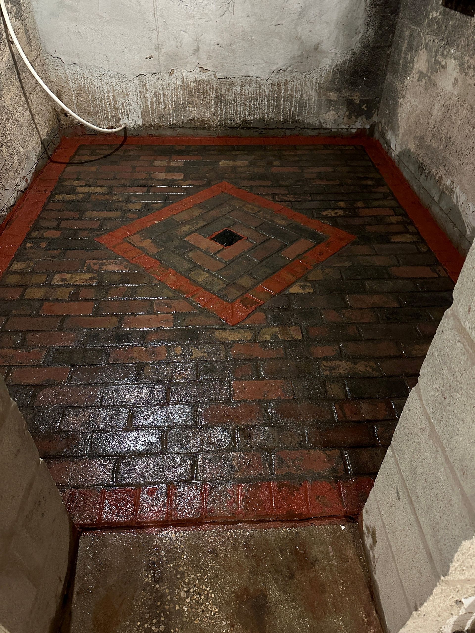 A room with a brick floor and a drain in the middle.