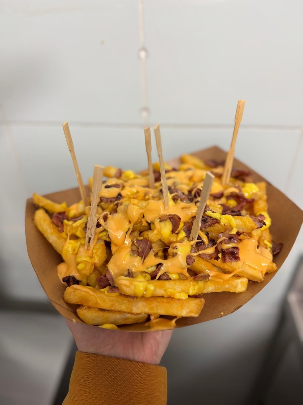 Una persona tiene in mano un vassoio di patatine fritte con formaggio e bacon.