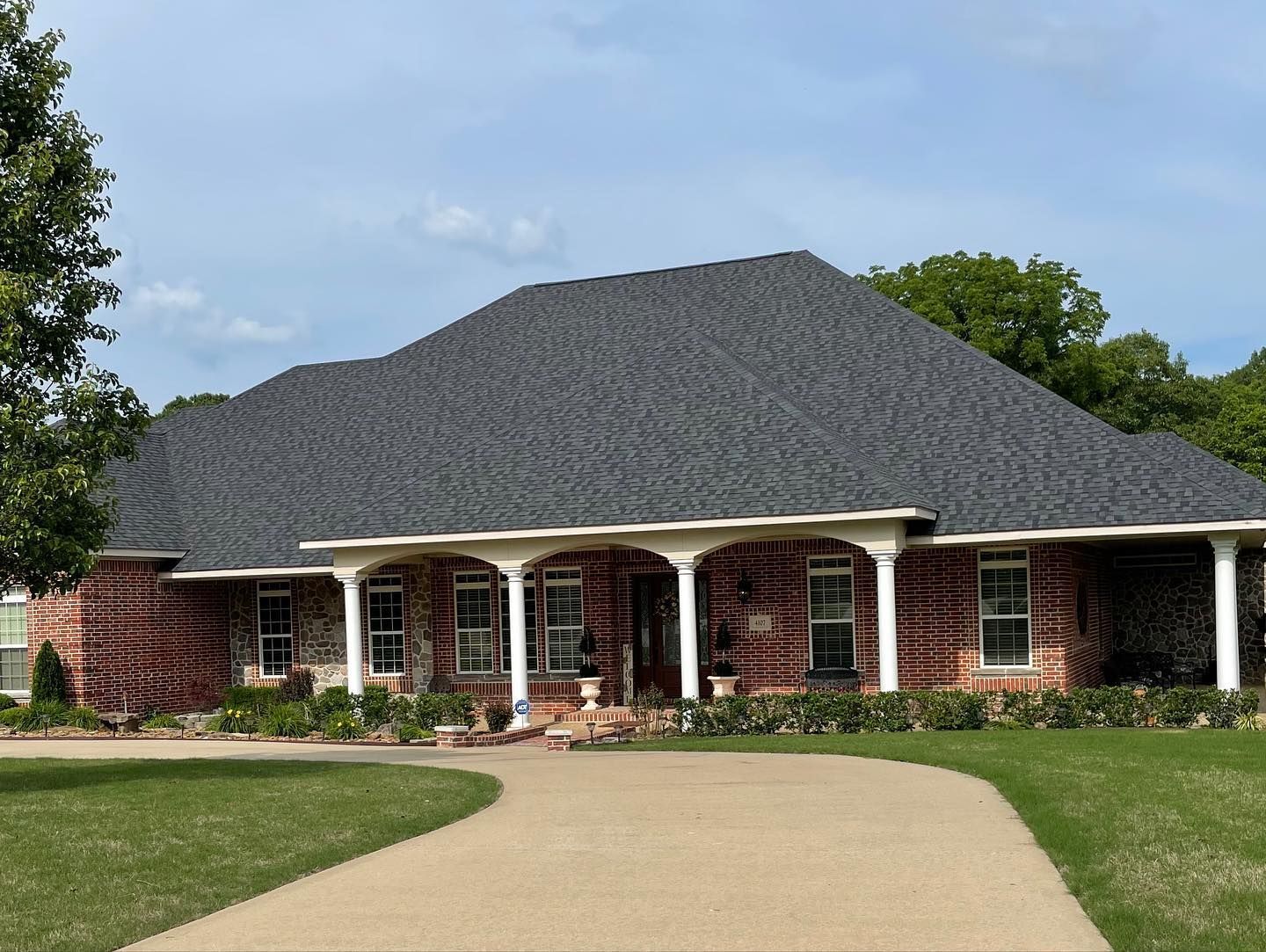 A large brick house with a gray roof and a driveway leading to it.