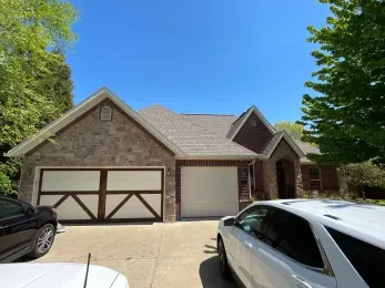 A white car is parked in front of a large brick house.