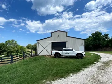 A white truck is parked in front of a barn.