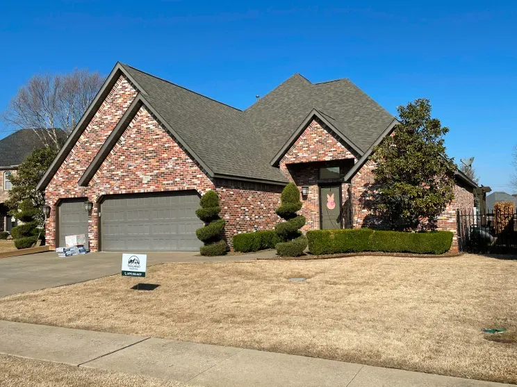 A large brick house with a gray garage door and a sign in front of it.