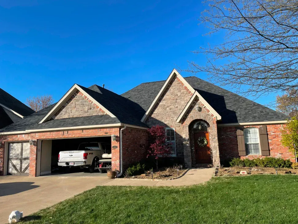 A brick house with a black roof and a truck parked in the driveway.