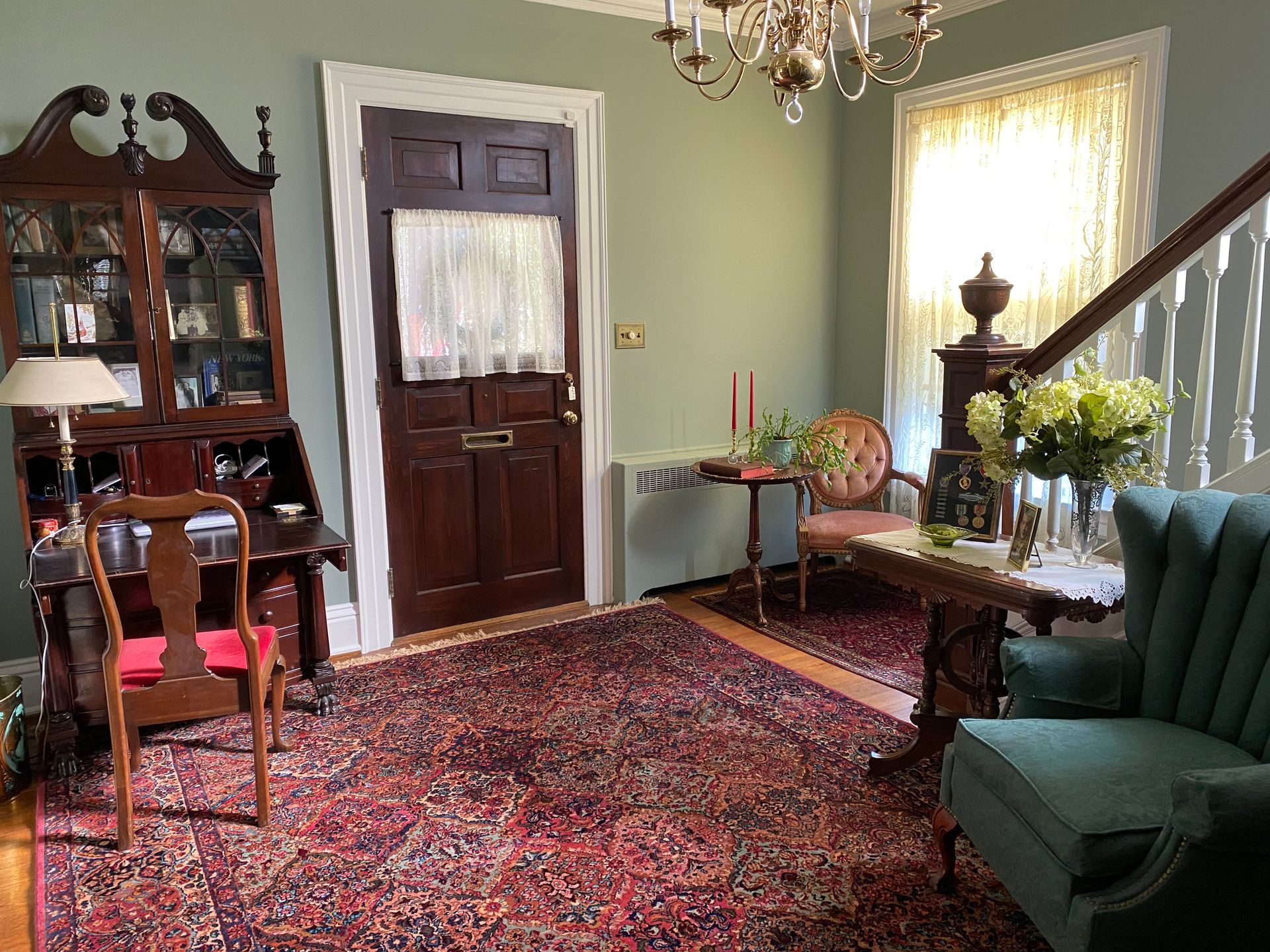 A living room with a rug , chairs , a desk and a chandelier.