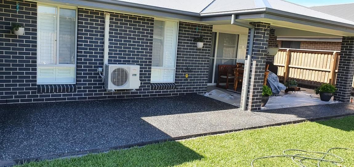 A Brick House With a Covered Patio and a Lawn in Front of It — MidCoast Concreting in Harrington, NSW