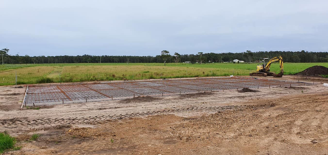A yellow excavator is working on a dirt field. — MidCoast Concreting in Mount George, NSW