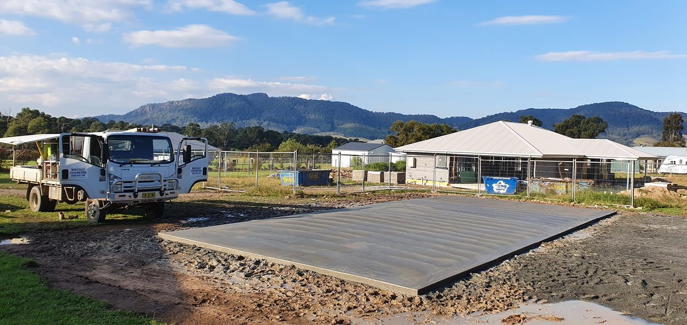 A truck is parked on a dirt road in front of a house under construction. — MidCoast Concreting in Mount George, NSW