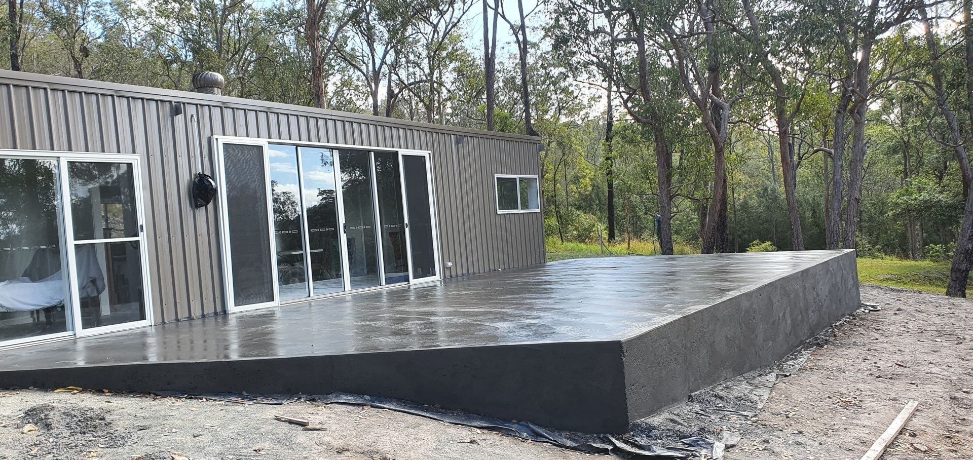 A house with a large concrete deck in front of it surrounded by trees. — MidCoast Concreting in Mount George, NSW
