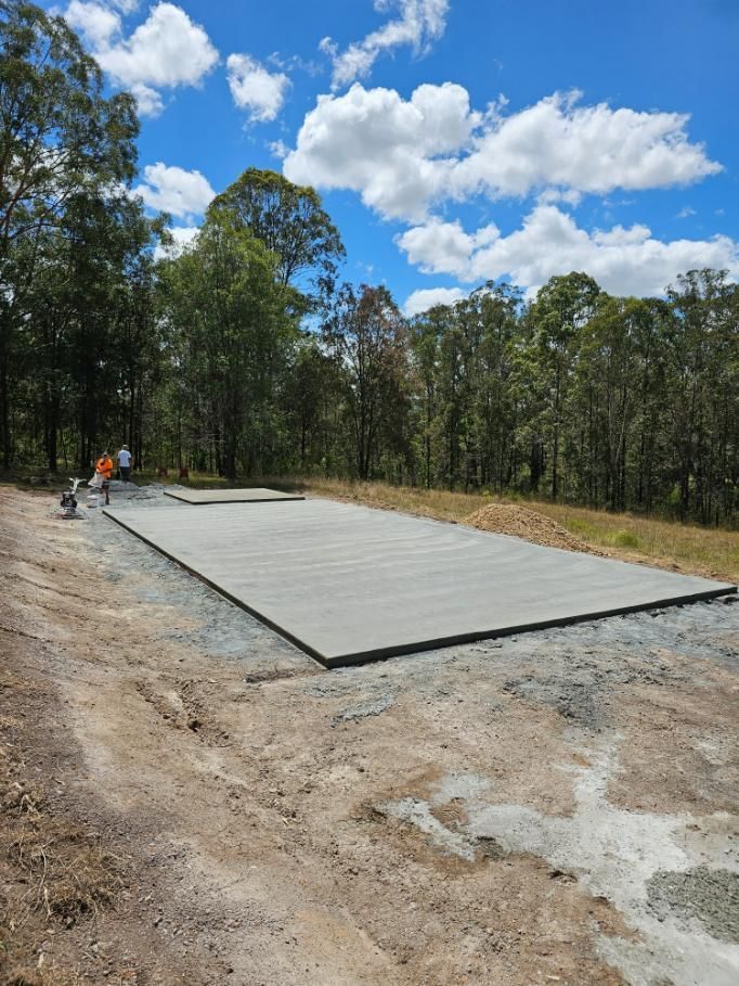 A Large Concrete Slab is Sitting in the Middle of a Dirt Field Surrounded by Trees — MidCoast Concreting in Mount George, NSW