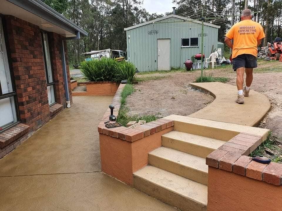 A man in an orange shirt is walking down a concrete sidewalk in front of a house — MidCoast Concreting in Mount George, NSW