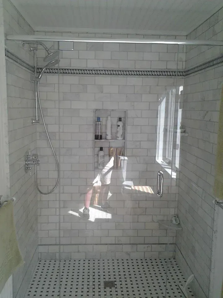 A shower with a glass door and white tiles.