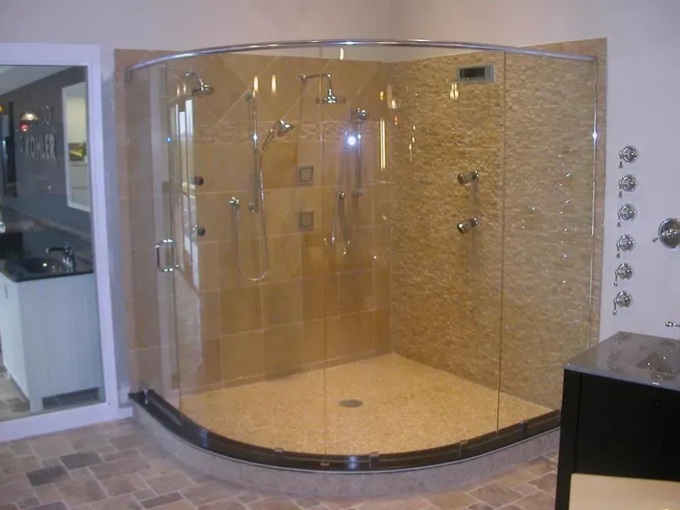 A bathroom with a walk in shower with a curved glass door.