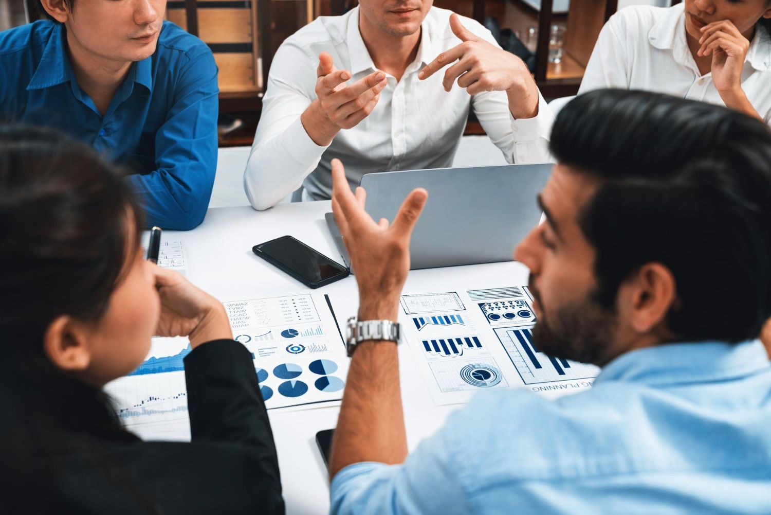 People in a meeting, discussing data analysis with charts and a laptop on a white table.
