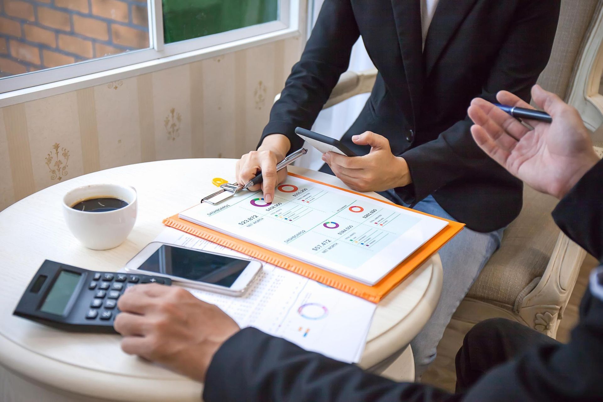 People reviewing documents at a table. Hands holding pens, charts and graphs visible.