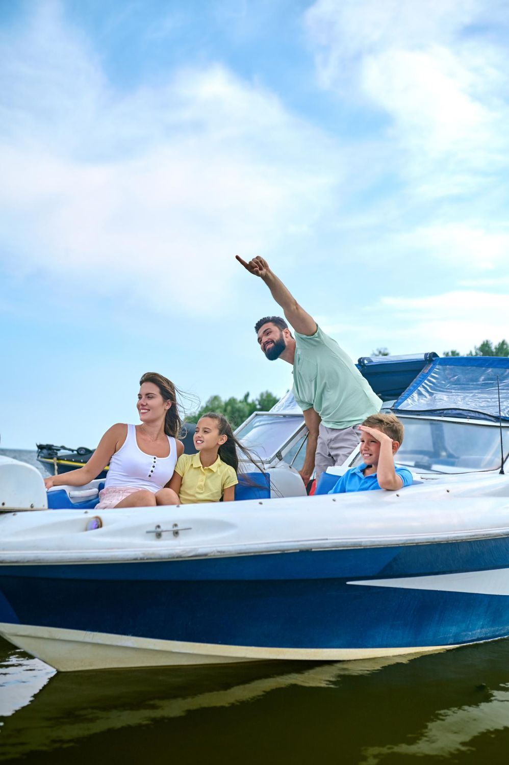 Family on a boat, man pointing upwards, woman smiling, children looking on, blue sky.
