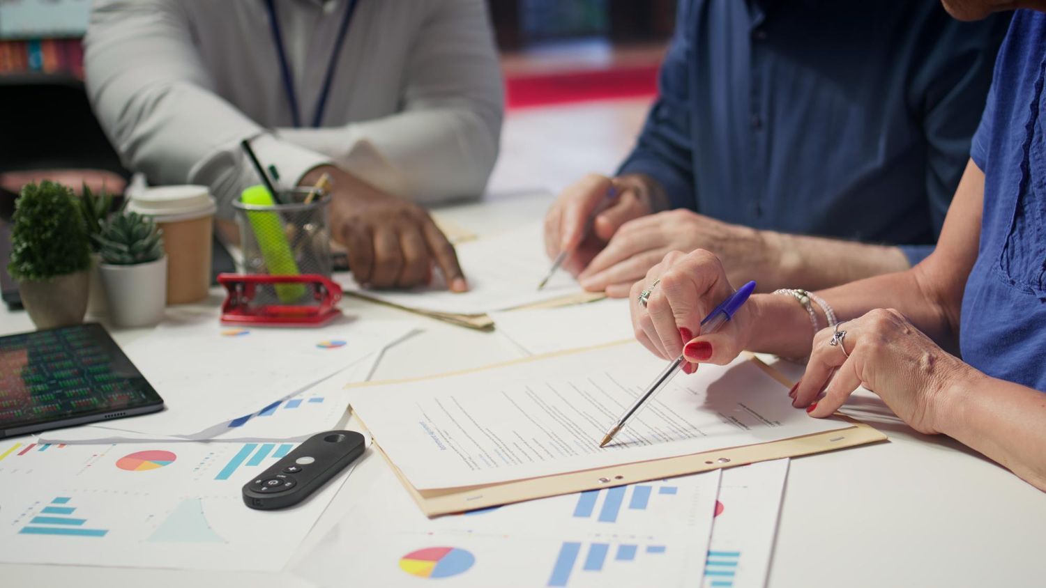 People reviewing documents at a table. Hands holding pens, charts and graphs visible.