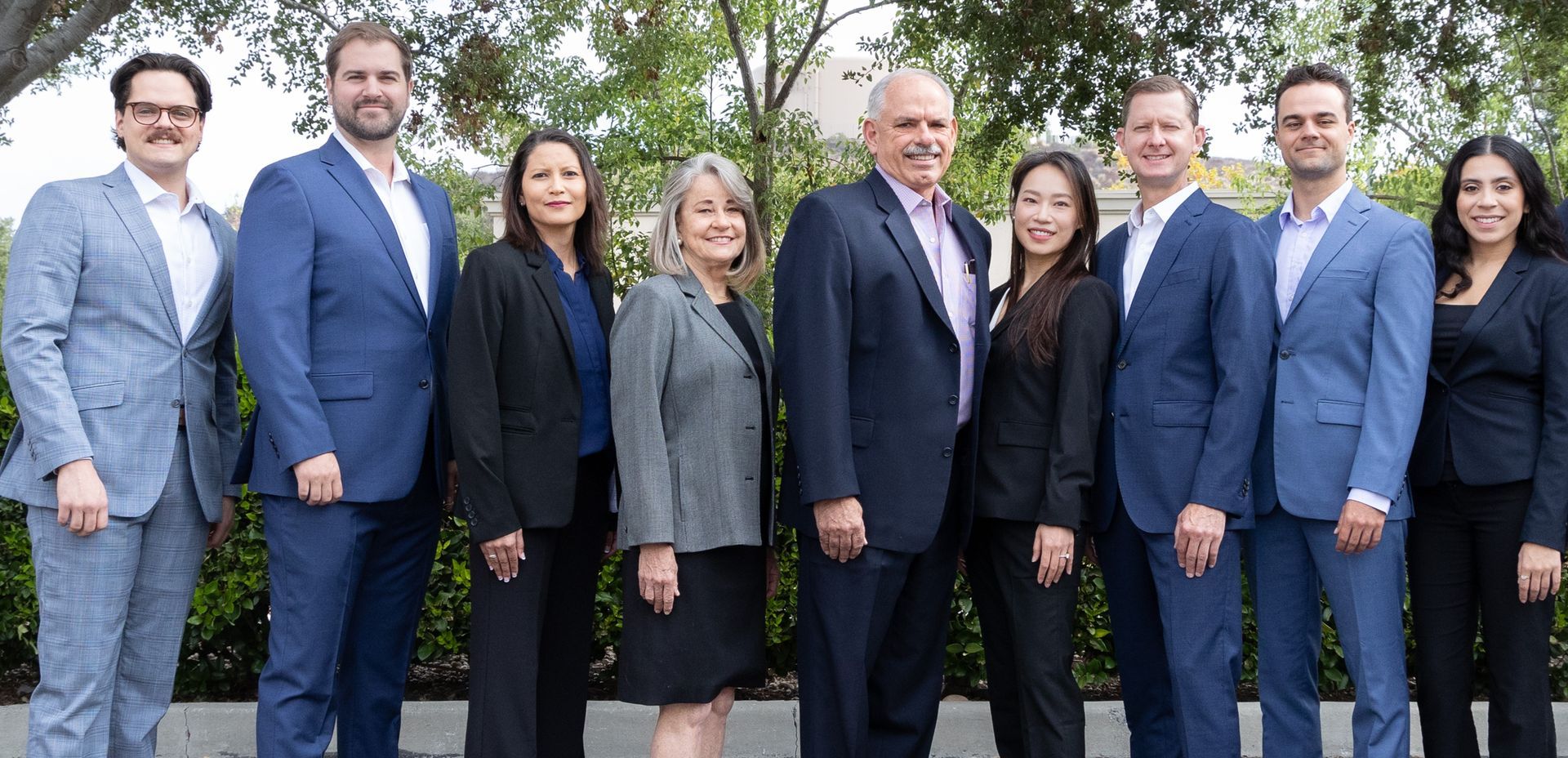 Group of nine people in professional attire posing outdoors.