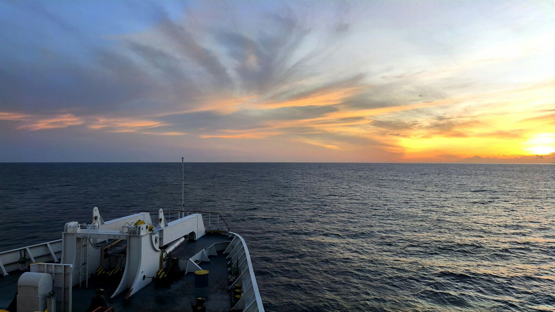 Man on shoreline watches a ship sail on choppy water. Overcast sky.