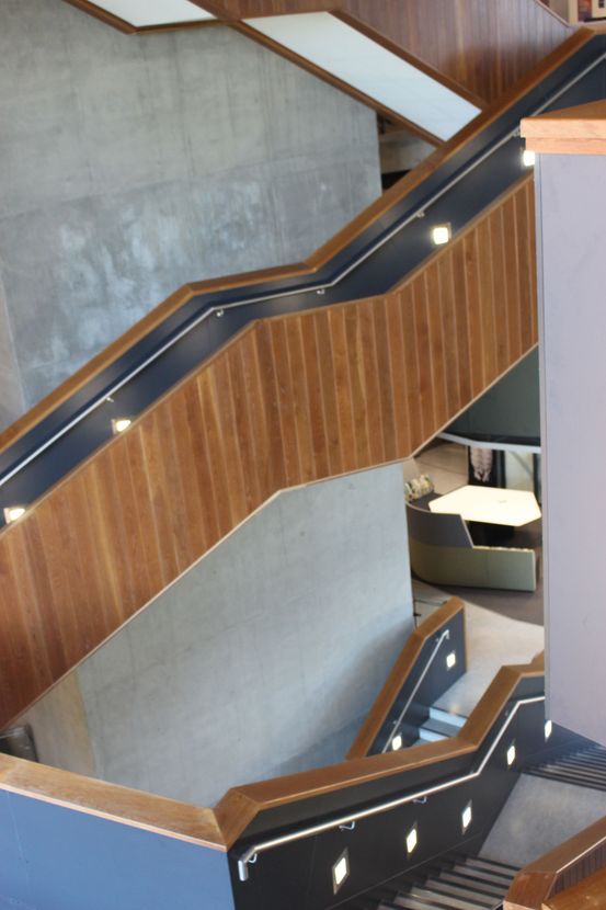Wooden staircase with black handrails and inset lights, leading to a seating area.