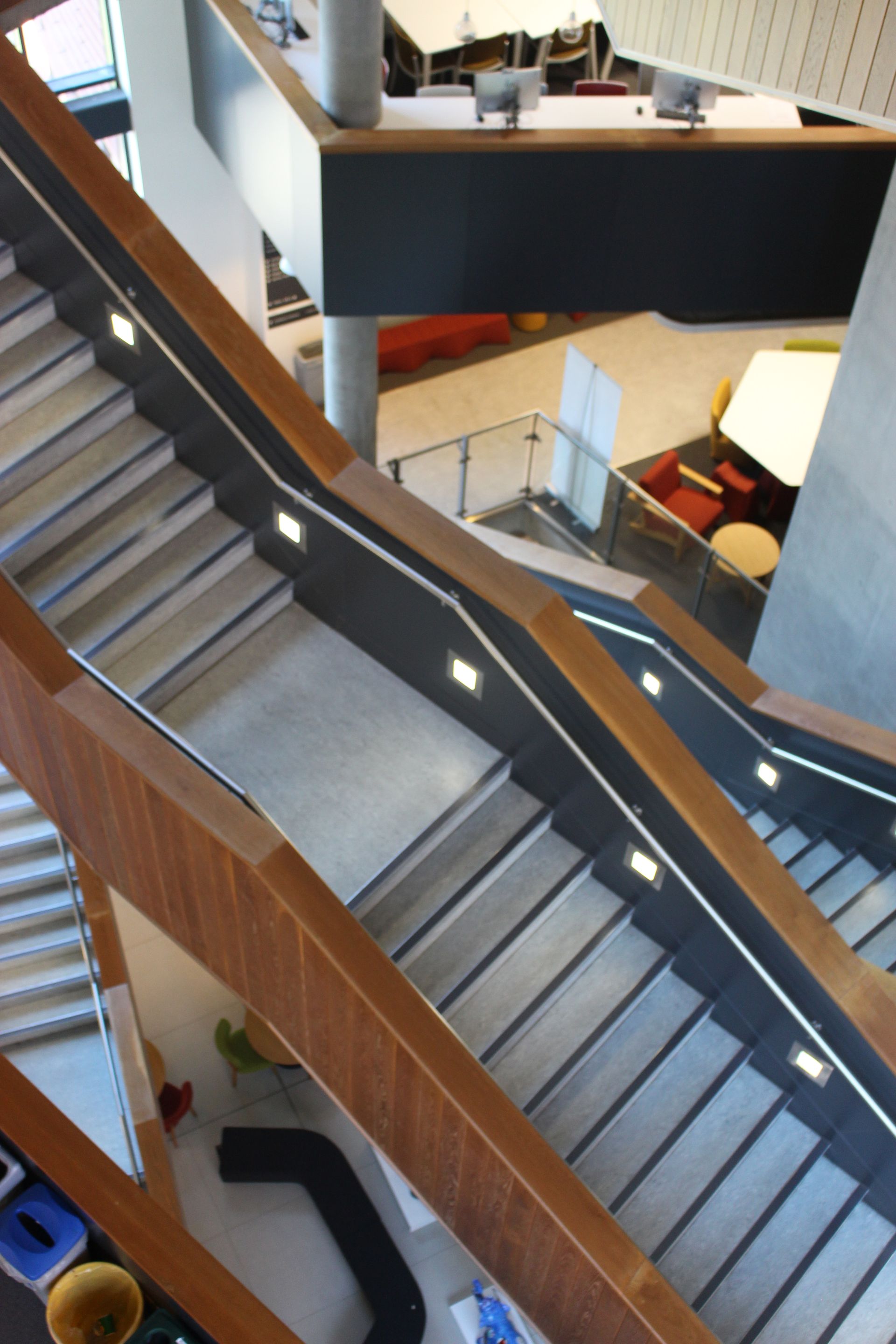Multi-level staircase with wood and black detailing, leading up and down in a modern building.