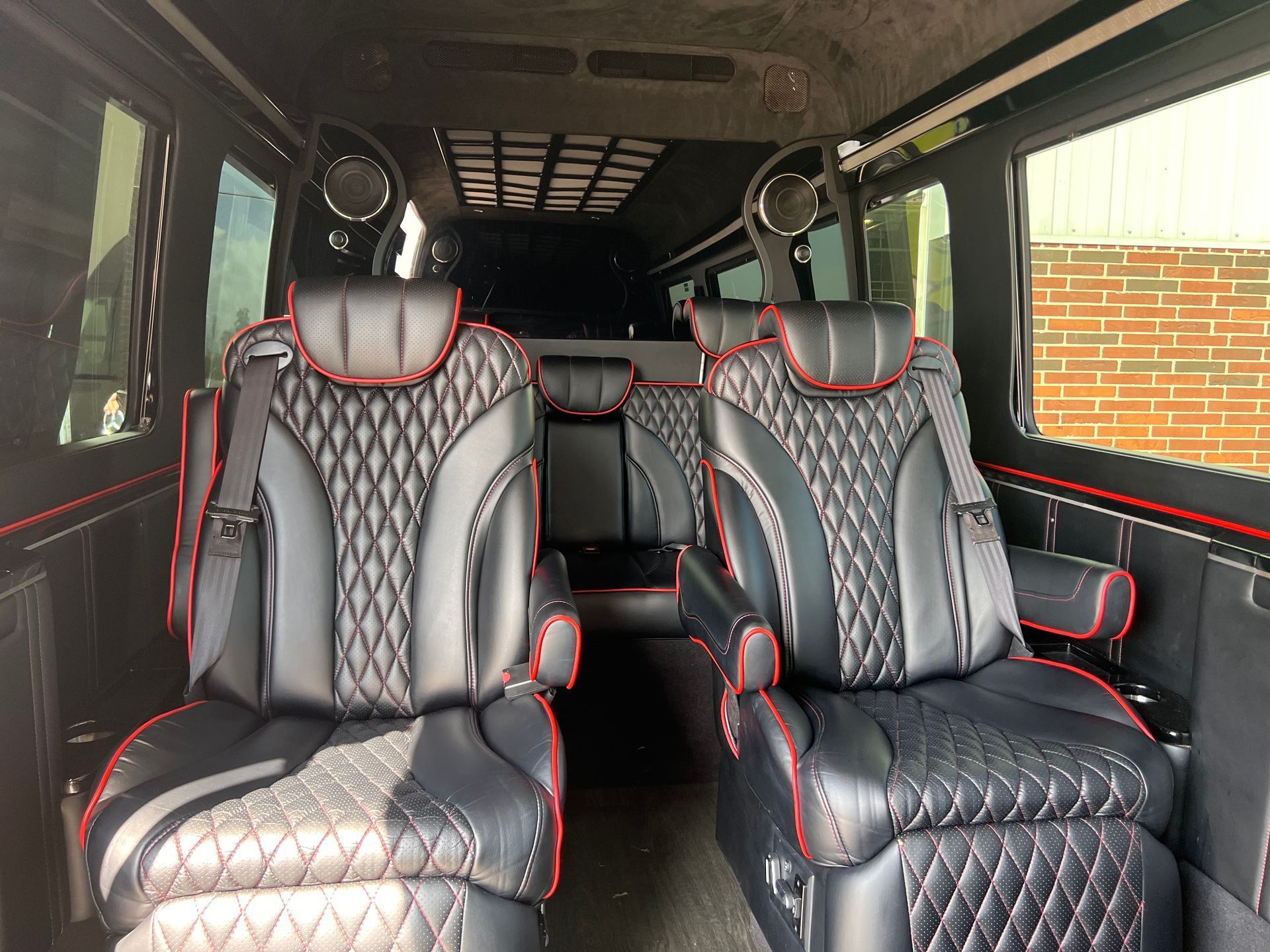 Interior of a luxury van with black leather seats, red stitching, and overhead speakers.