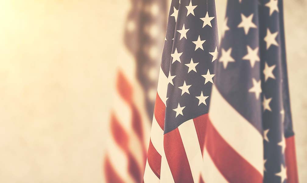 A woman is holding an american flag and a rose at a funeral.