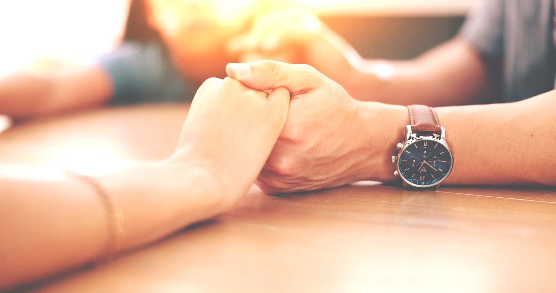 A man and a woman are holding hands over a wooden table.
