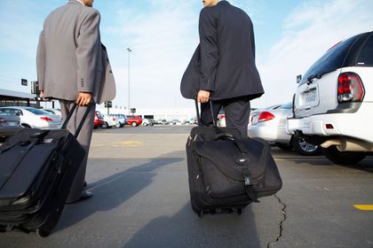 Due uomini trascinano le valigie in un parcheggio