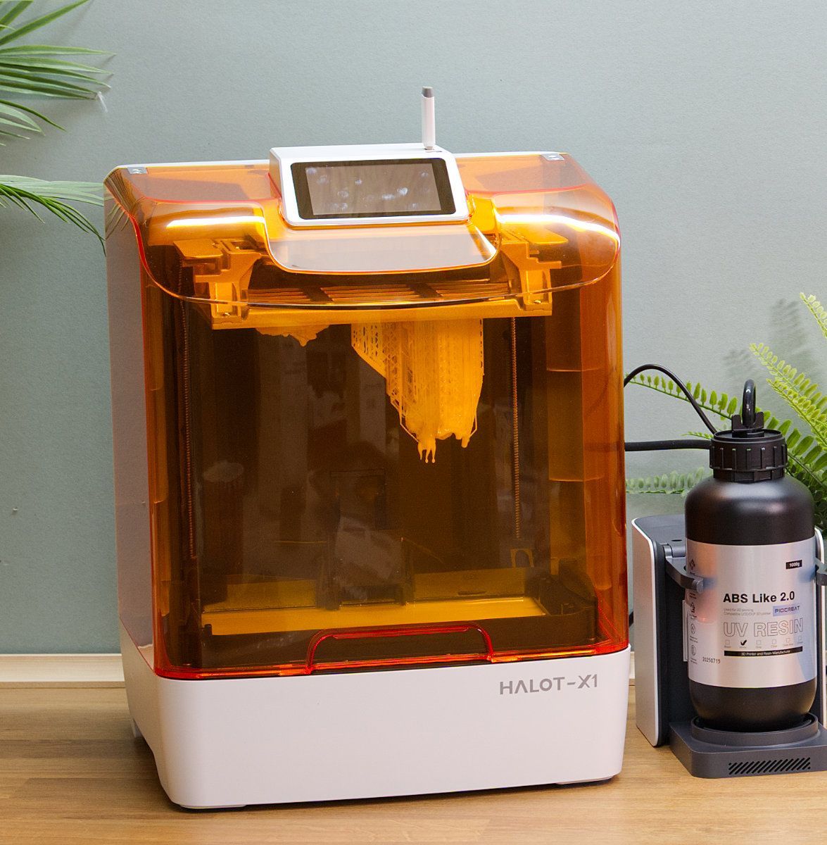 A resin 3D printer with an orange cover and a screen, beside a bottle of resin and a black base.