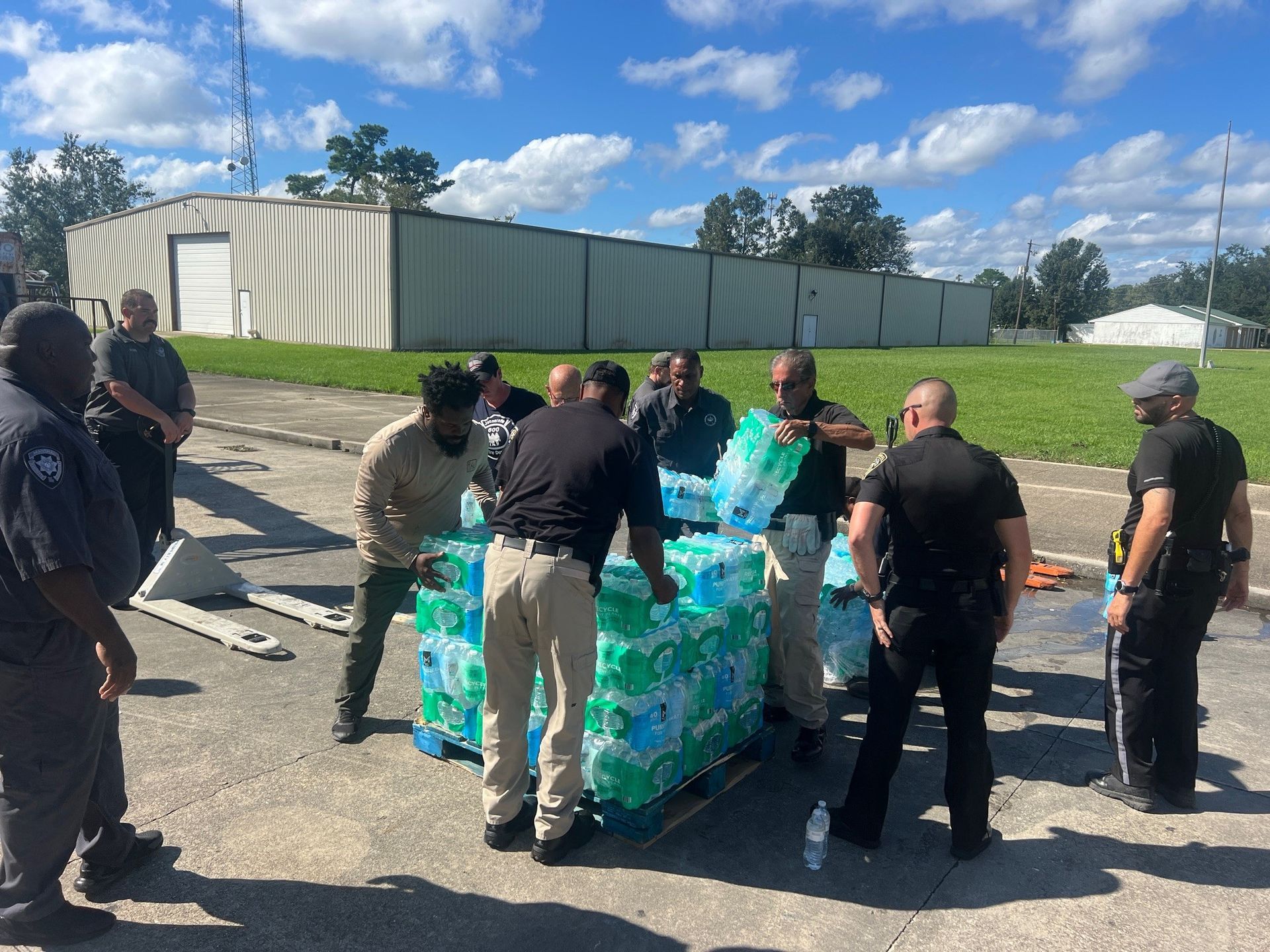A group of men are standing around a pallet of water bottles.